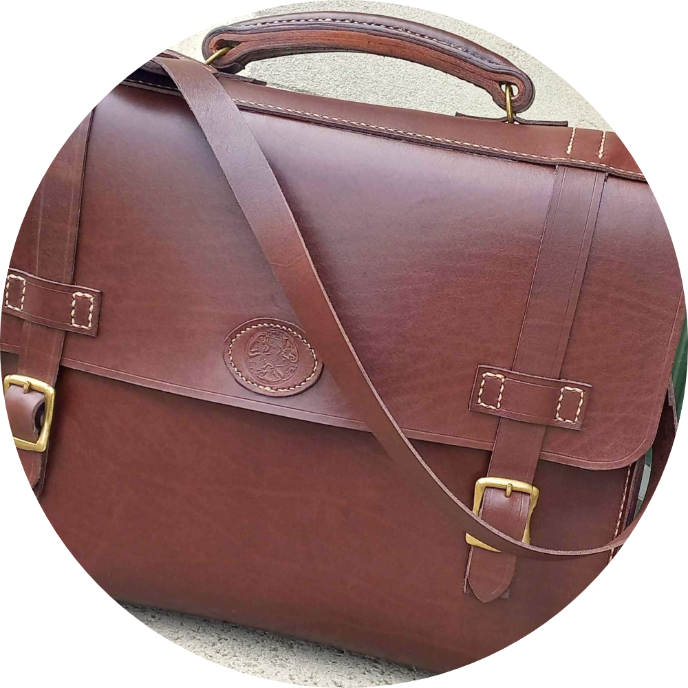 A messenger bag hand-made with chocolate brown leather and gold hardware, stamped with the Albannach Crafts logo.
