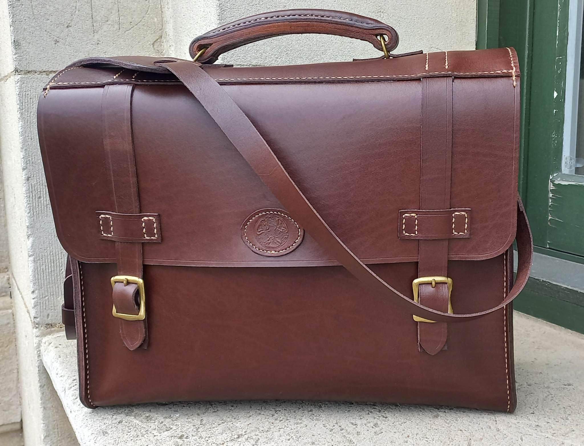 A messenger bag hand-made with chocolate brown leather and gold hardware, stamped with the Albannach Crafts logo.