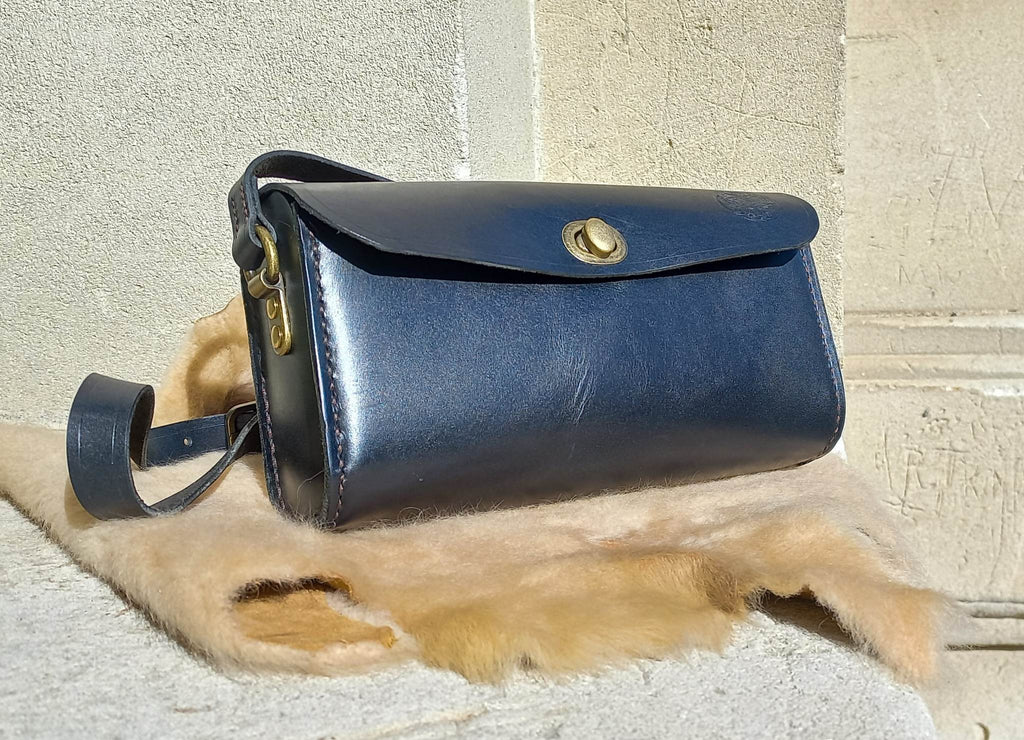 Maggie Shoulder Bag made from tannery-dyed vegetable-tanned cowhide with brass hardware, placed atop a wool rug outdoors.
