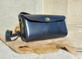 Maggie Shoulder Bag made from tannery-dyed vegetable-tanned cowhide with brass hardware, placed atop a wool rug outdoors.