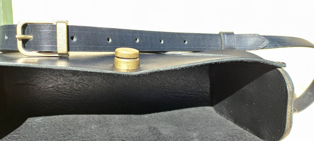 The internal pocket of the Maggie Shoulder Bag made from tannery-dyed vegetable-tanned cowhide with brass hardware, placed atop a wool rug outdoors.