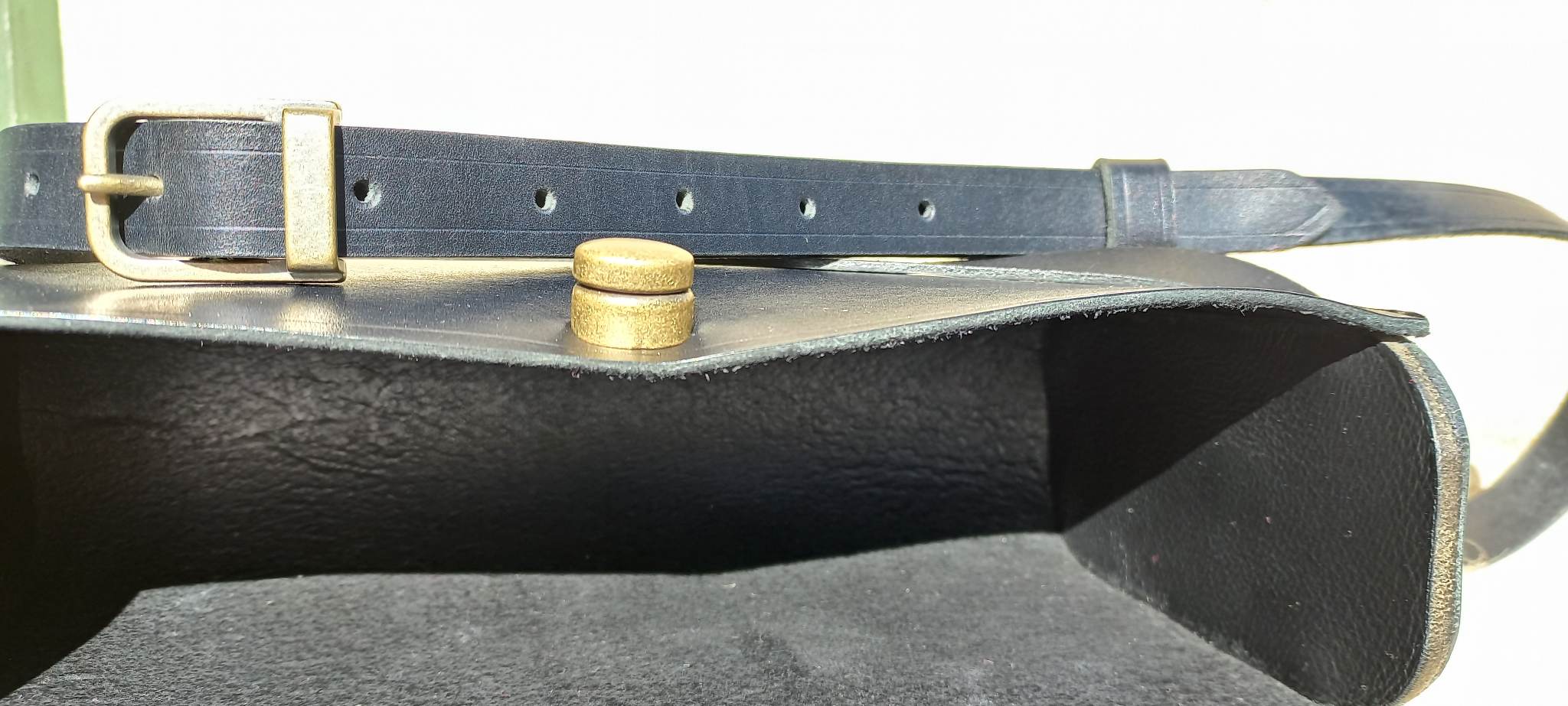 The internal pocket of the Maggie Shoulder Bag made from tannery-dyed vegetable-tanned cowhide with brass hardware, placed atop a wool rug outdoors.