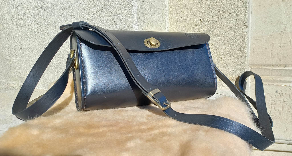 Maggie Shoulder Bag made from tannery-dyed vegetable-tanned cowhide with brass hardware, placed atop a wool rug outdoors, showcasing the long shoulder strap.