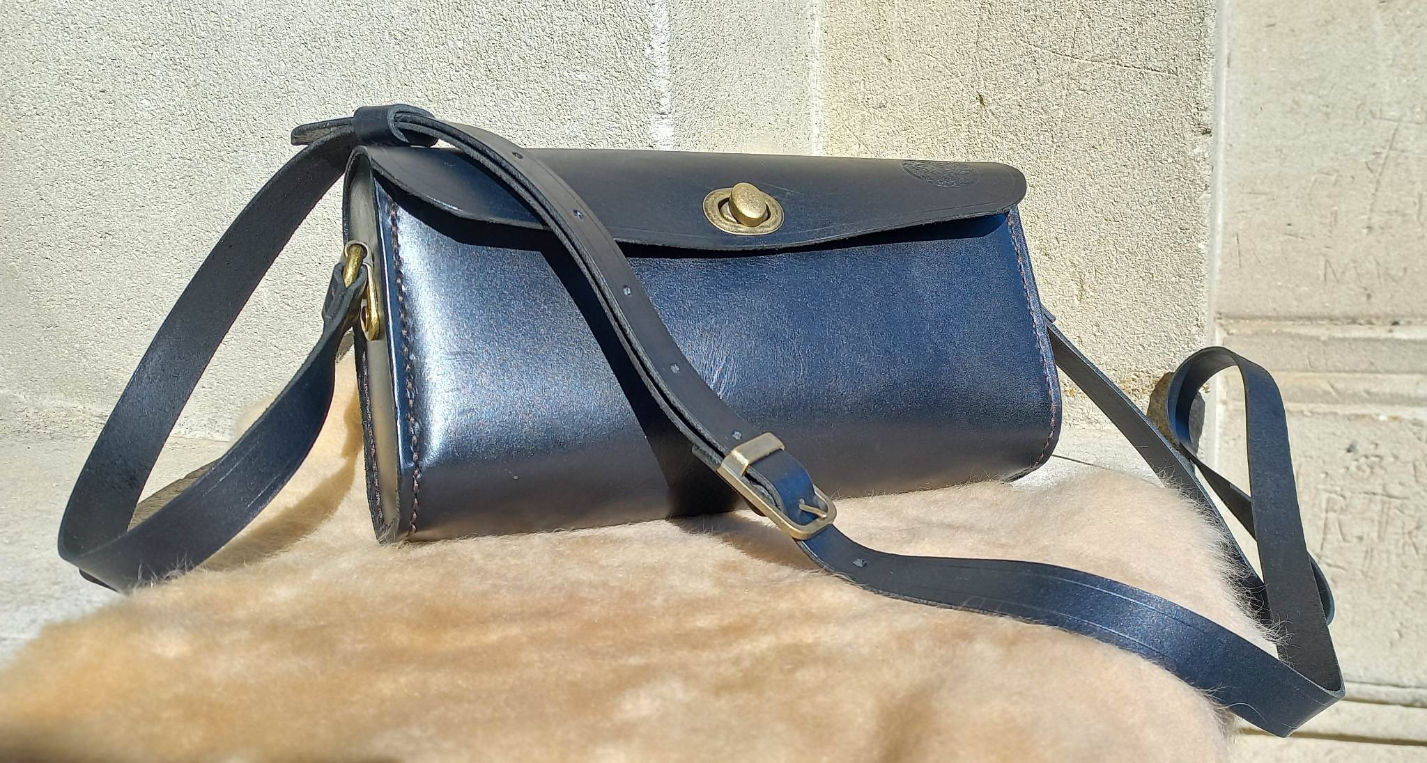 Maggie Shoulder Bag made from tannery-dyed vegetable-tanned cowhide with brass hardware, placed atop a wool rug outdoors, showcasing the long shoulder strap.