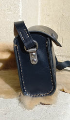 Side view of the Maggie Shoulder Bag made from tannery-dyed vegetable-tanned cowhide with brass hardware, placed atop a wool rug outdoors.