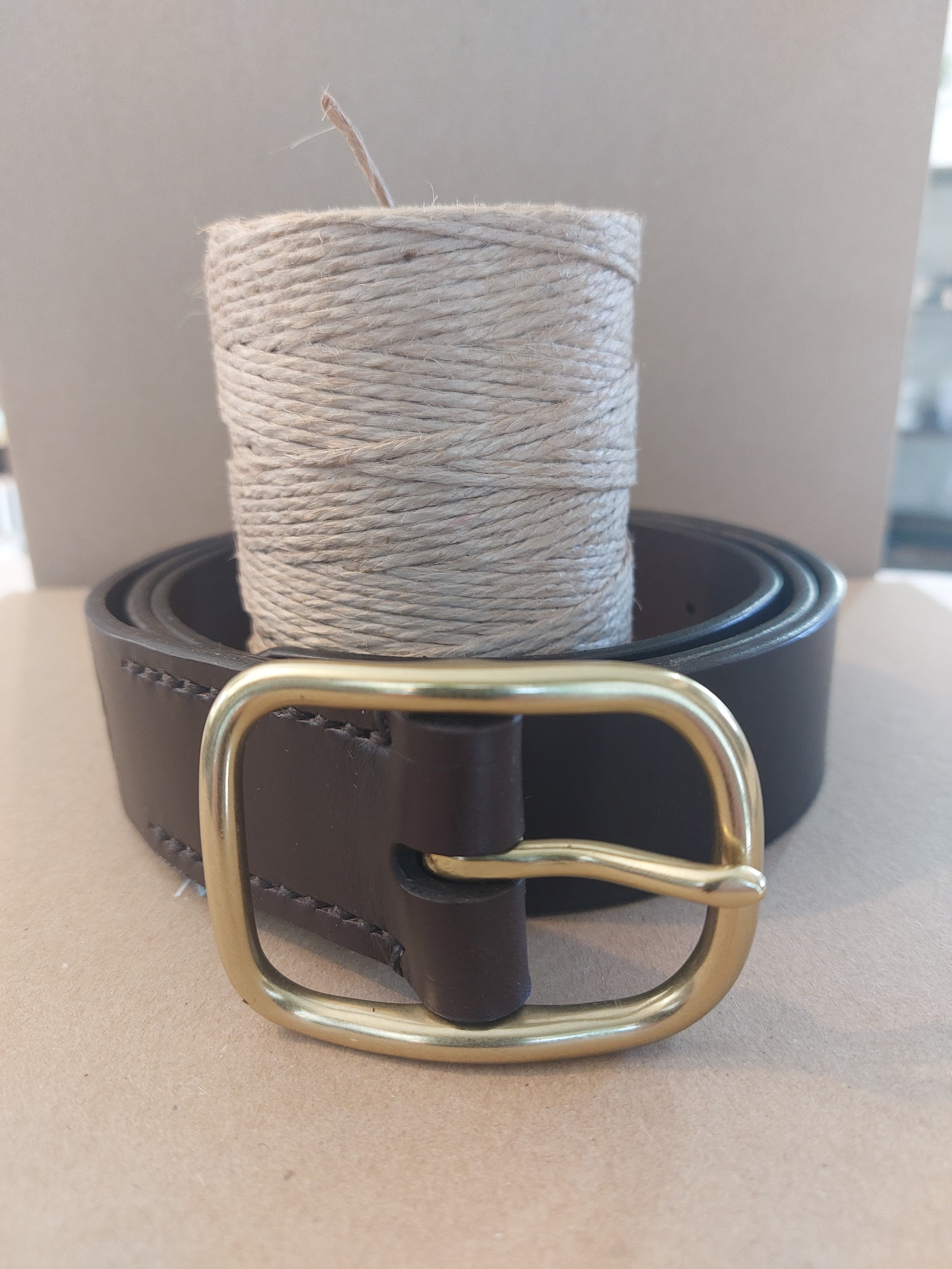 Brown Leather Belt - 46"/117cm handmade with brown leather, complete with the Albannach Crafts logo and a solid brass buckle. Shown coiled around a spool of thread for scale.