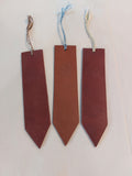 Bookmark made from brown vegetable-tanned leather, with a hand-plaited tassel at the top, stamped with the Albannach Crafts logo.