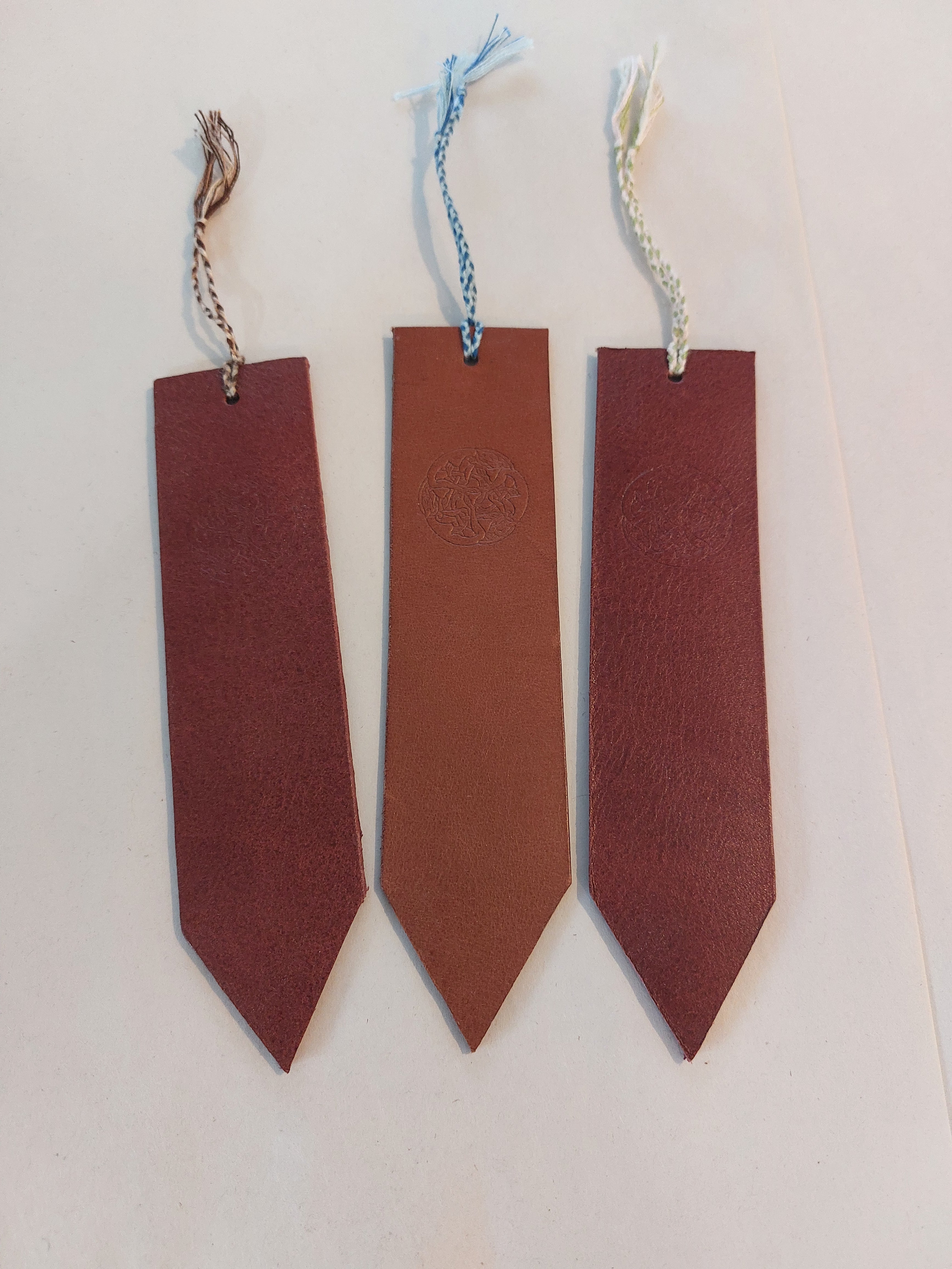 Bookmark made from brown vegetable-tanned leather, with a hand-plaited tassel at the top, stamped with the Albannach Crafts logo.