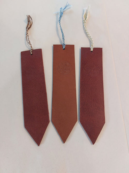 Bookmark made from brown vegetable-tanned leather, with a hand-plaited tassel at the top, stamped with the Albannach Crafts logo.