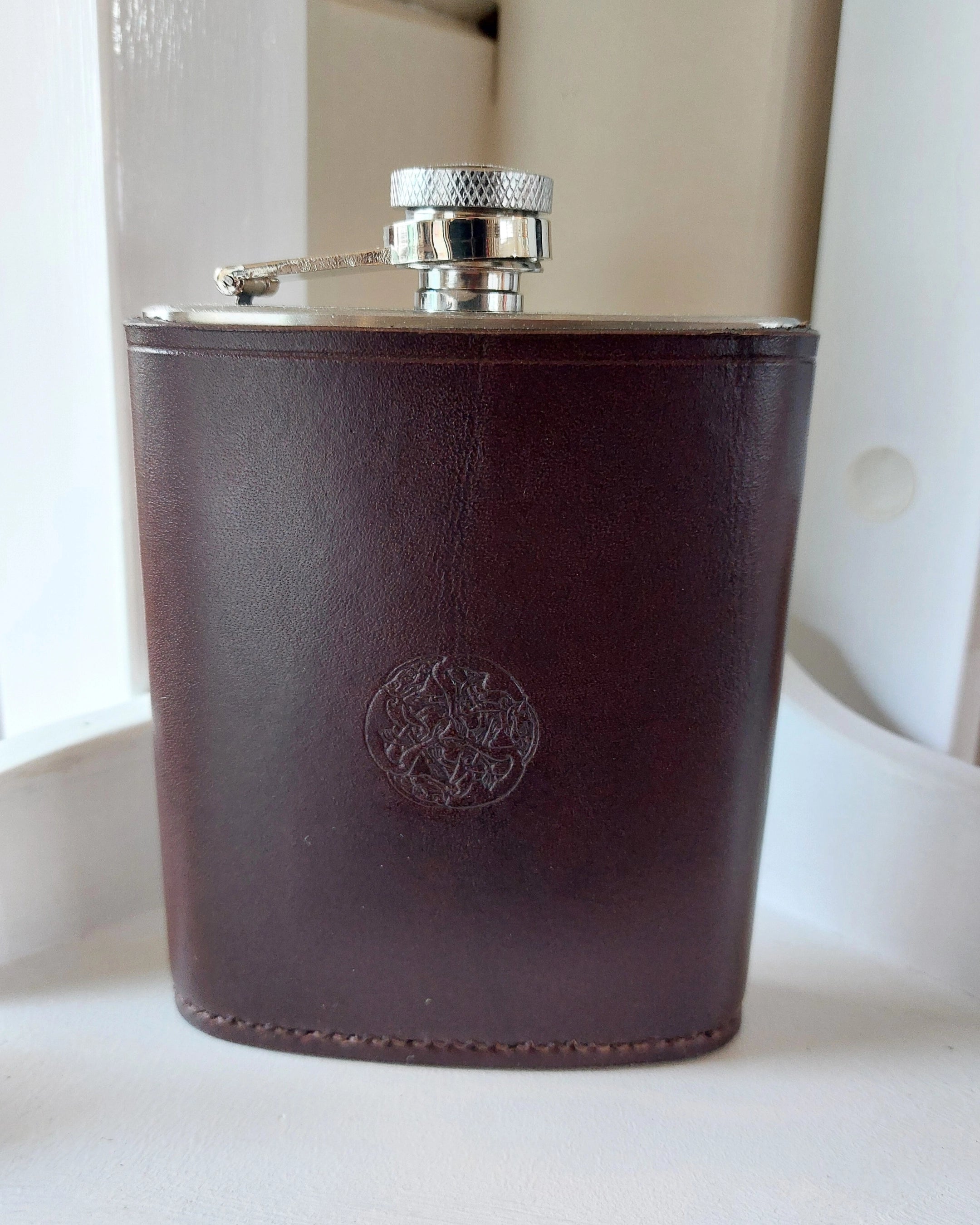 Silver alcohol flask cover case hand-made with dark brown leather and stamped with the Albannach Crafts logo.