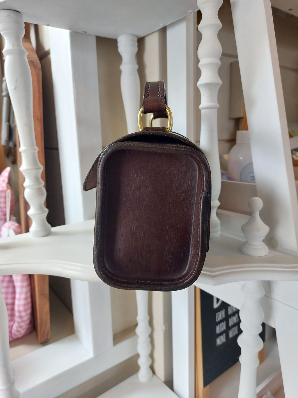 Side view of the Excelsior Hand Bag made from quality Italian rich brown leather, complete with solid brass hardware, sits atop a white shelf. Stamped with the Albannach Crafts logo.