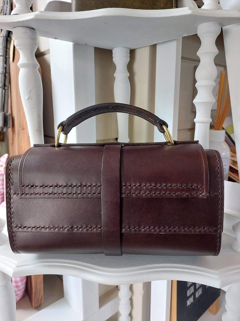 Back view of the Excelsior Hand Bag made from quality Italian rich brown leather, complete with solid brass hardware, sits atop a white shelf. Stamped with the Albannach Crafts logo.