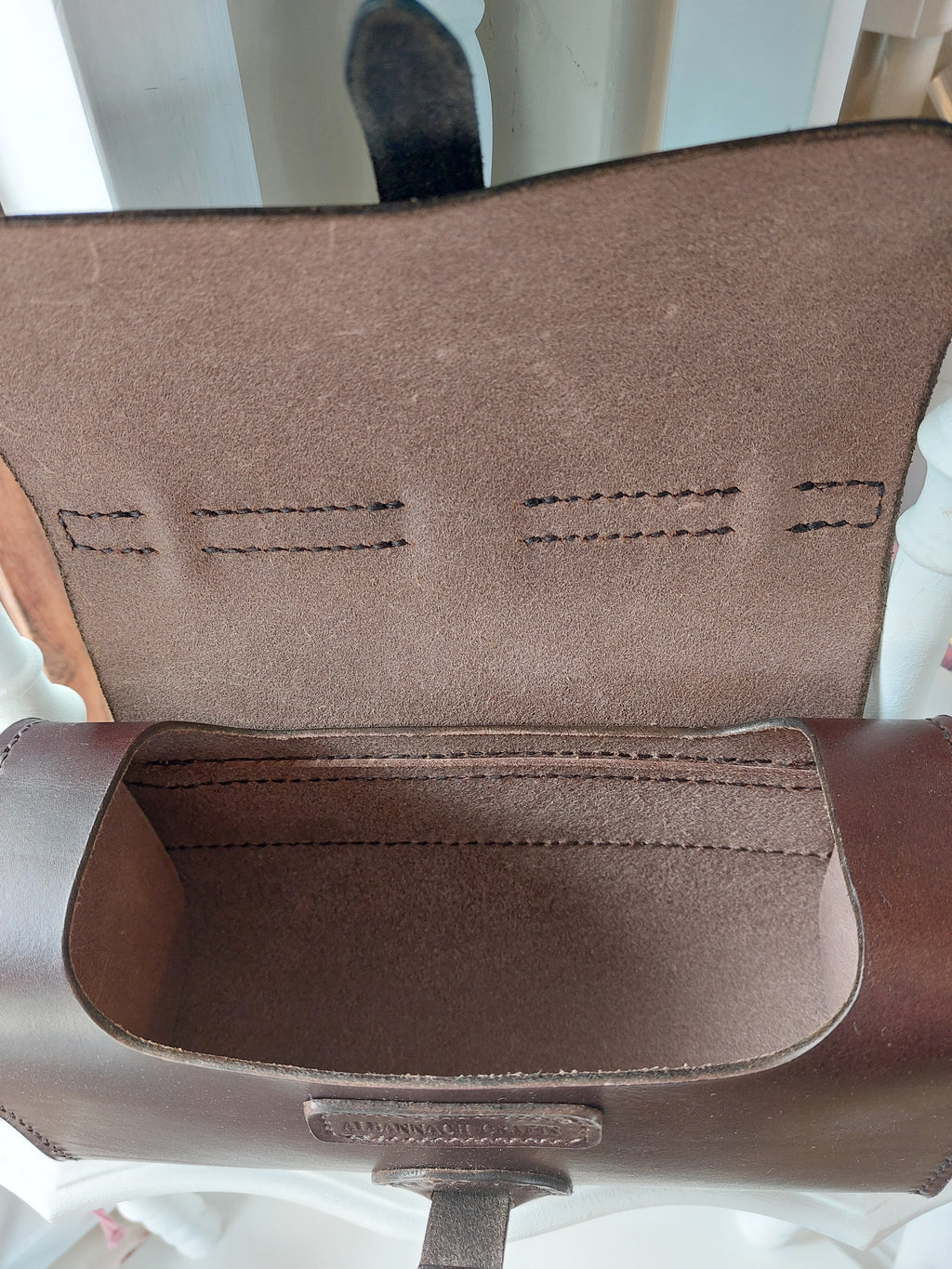 Internal view of the Excelsior Hand Bag made from quality Italian rich brown leather, complete with solid brass hardware, sits atop a white shelf. Stamped with the Albannach Crafts logo.