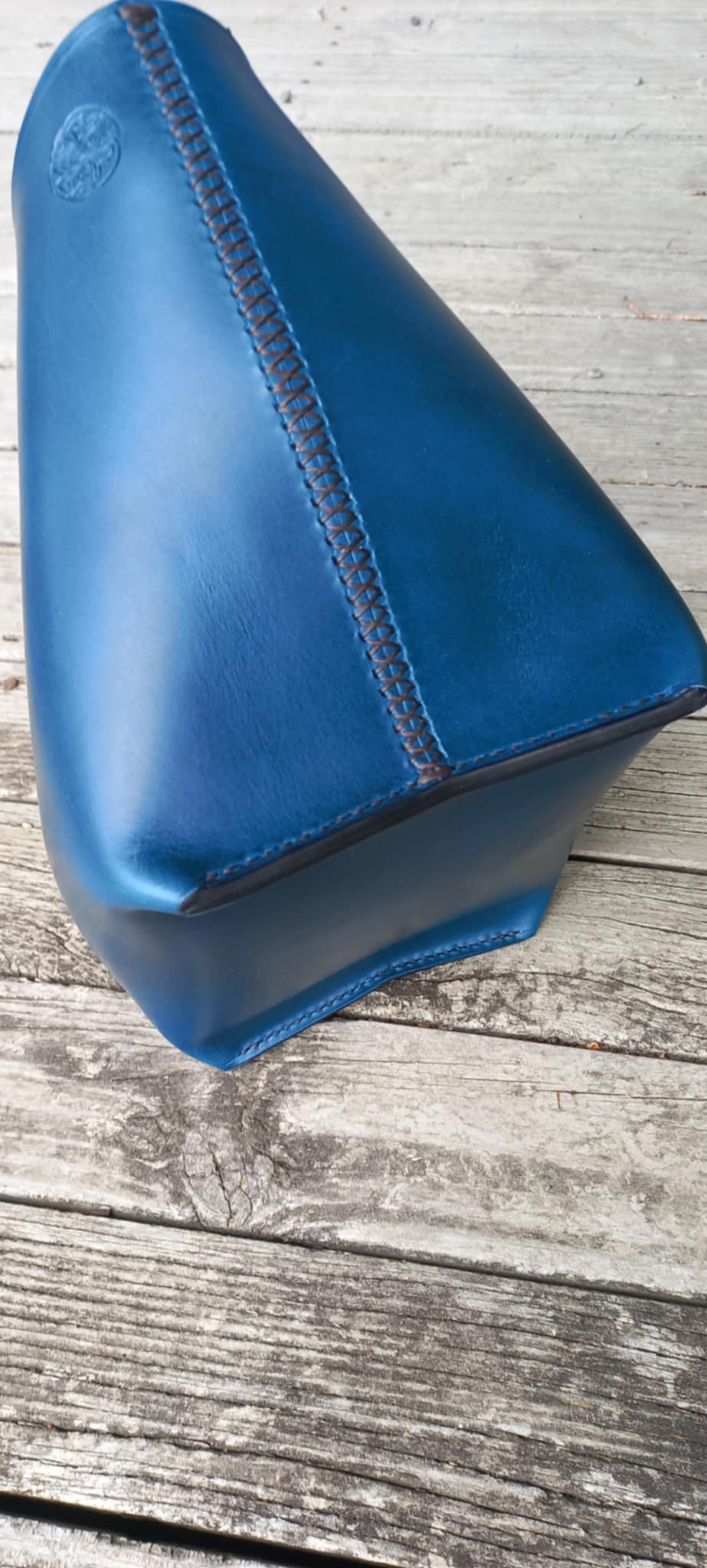 The bottom of the OTT Midi Tote bag made with a vibrant blue vegetable-tanned Italian leather, placed on a wooden verandah.