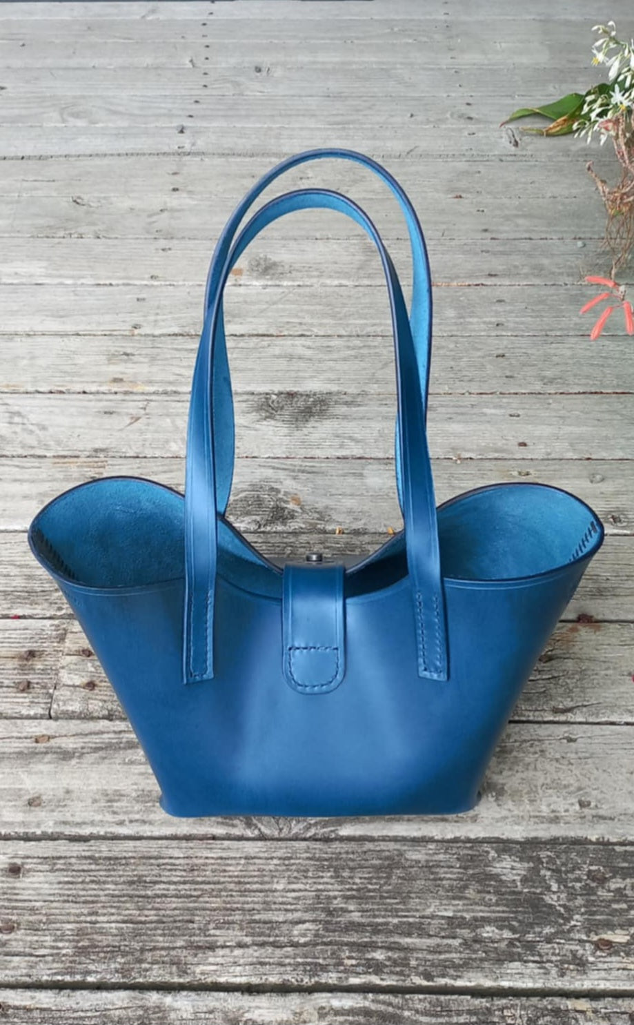 The back of the OTT Midi Tote bag made with a vibrant blue vegetable-tanned Italian leather, placed on a wooden verandah.