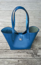 OTT Midi Tote bag made with a vibrant blue vegetable-tanned Italian leather, placed on a wooden verandah.