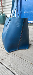 The side of the OTT Midi Tote bag made with a vibrant blue vegetable-tanned Italian leather, placed on a wooden verandah.