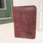 Passport Wallet made with quality brown vegetable-tanned leather, placed outside a historic cottage.