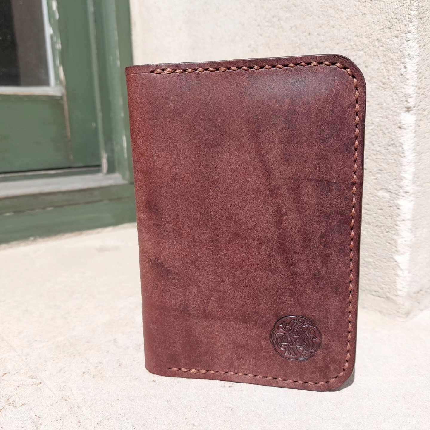 Passport Wallet made with quality brown vegetable-tanned leather, placed outside a historic cottage.