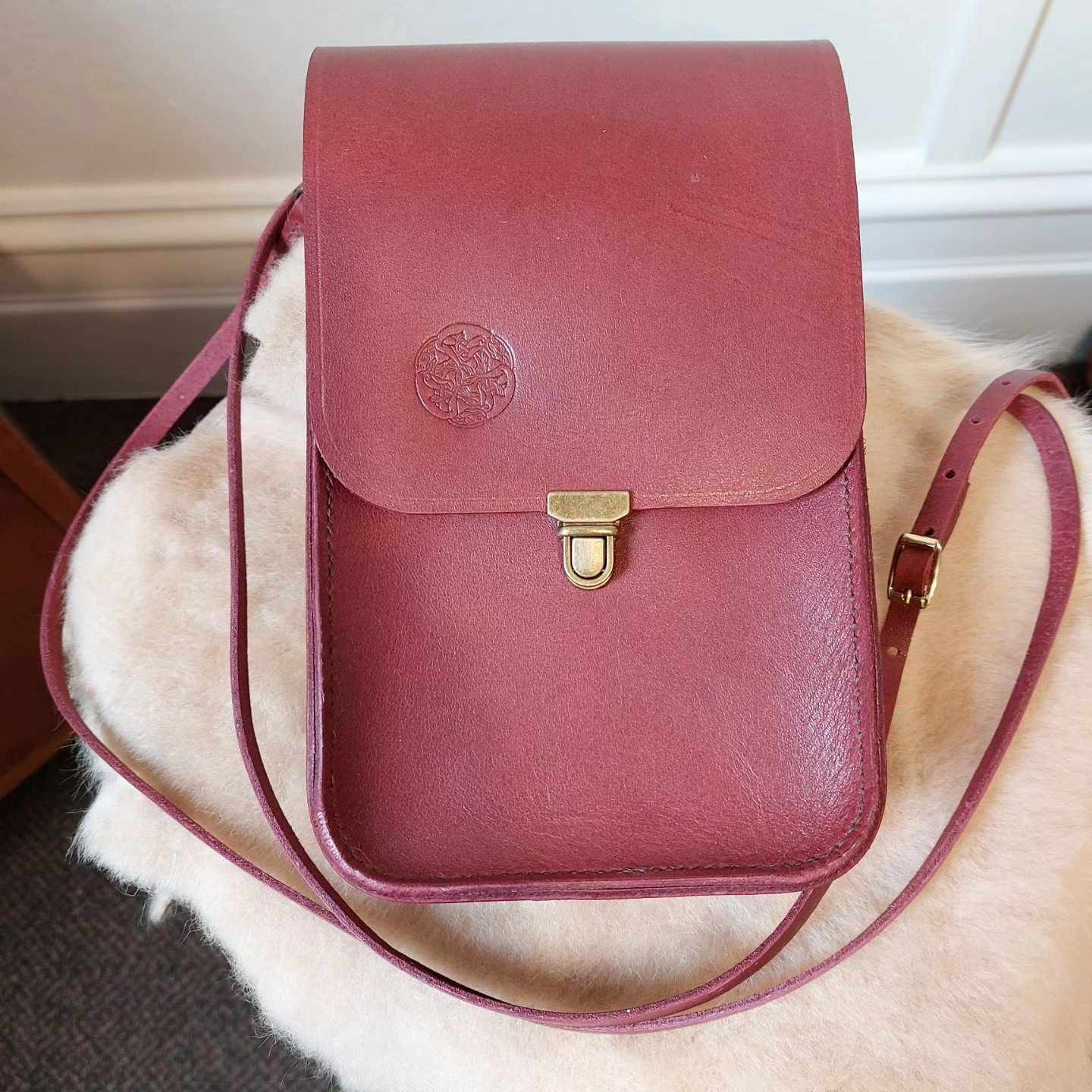 Small shoulder bag with gold hardware, hand-made with red dyed leather, placed atop a sheepskin.