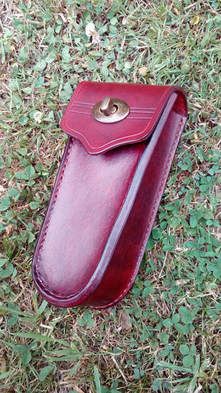 A tool sheath hand-made from red dyed leather with a gold clasp, placed on a lawn.