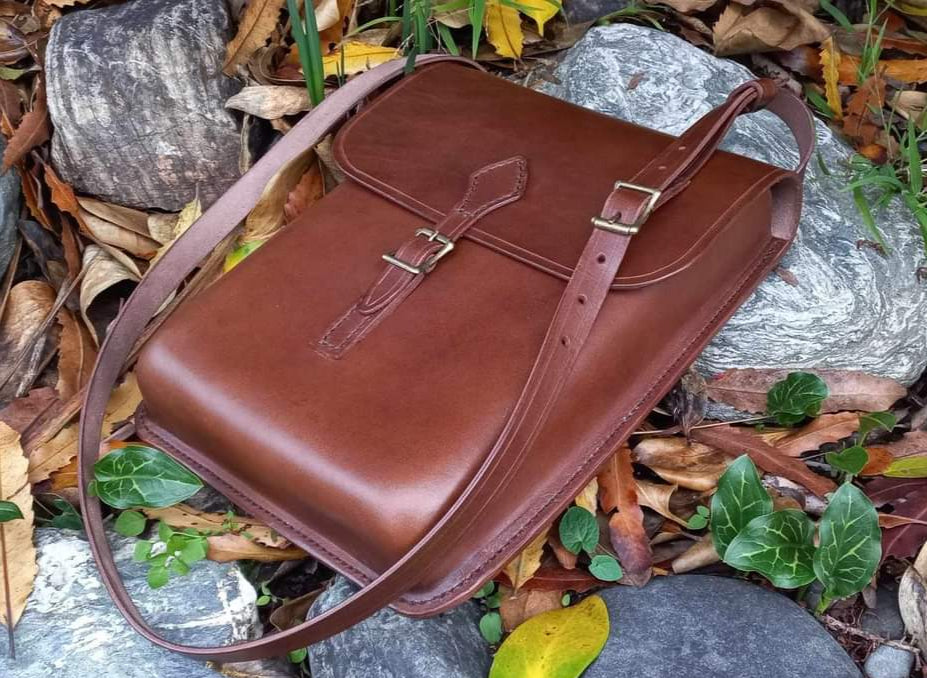 Wet Formed Shoulder Bag made from quality Italian vegetable-tanned leather, complete with shoulder strap, leans against some rocks amongst the autumn leaves.